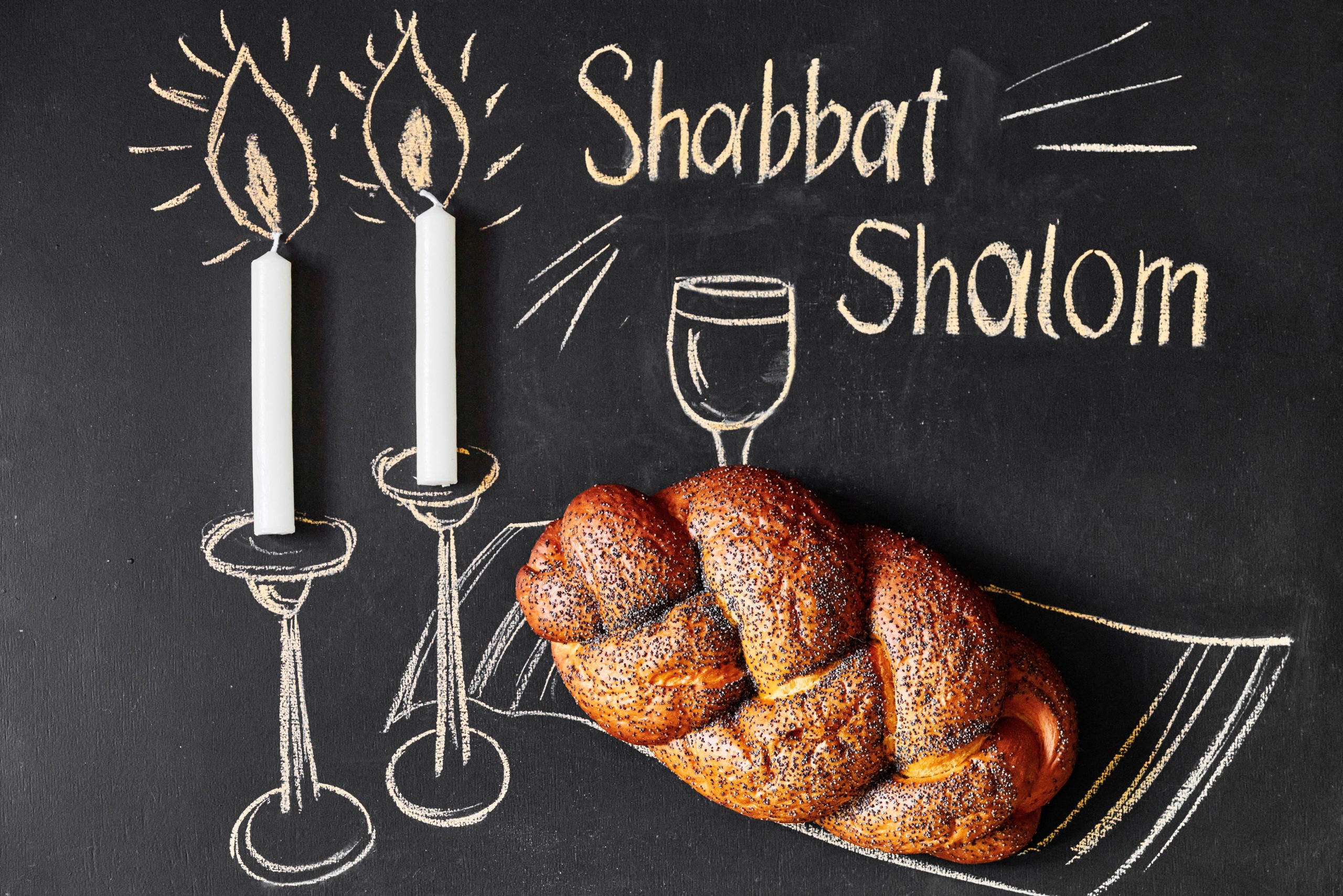 Shabbat Shalom - Jewish and Hebrew greetings. Candles and a glass of wine drawn on a chalk board next to wicker bread Shabbat Shalom - Jewish and Hebrew greetings. Candles and a glass of wine drawn on a chalk board next to wicker bread